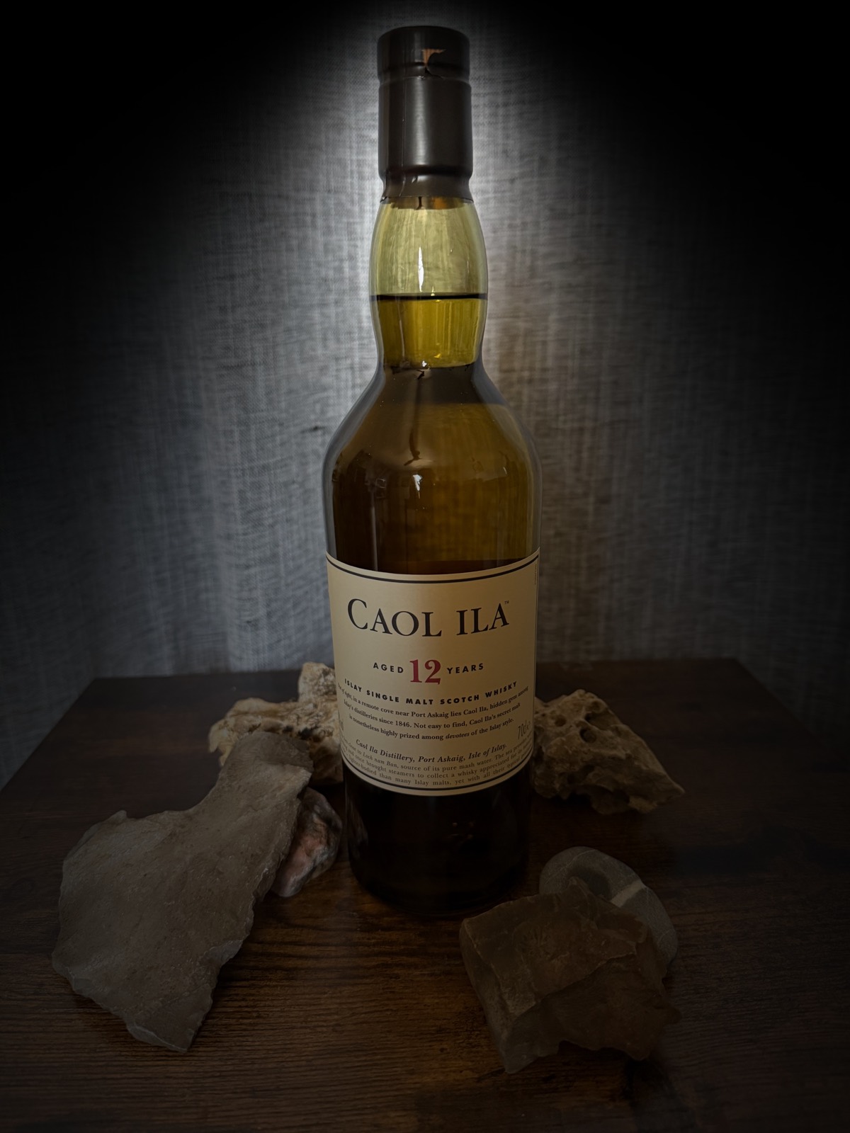 Caol Ila 12 Year Old Islay single malt bottle under a discreet spotlight among grey stones